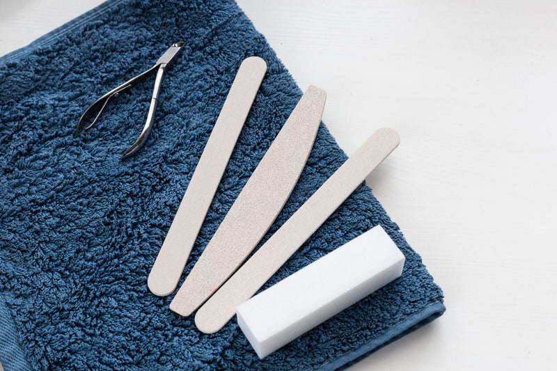 Nail files, a buffing block and clippers laid on a folded towel, the tools used to manage thickened toenails