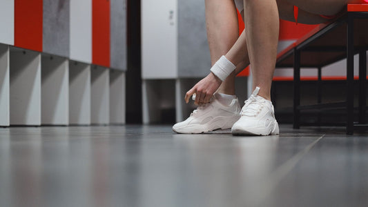 Person changing into trainers on a bench in a locker room, illustrating an article on whole-body deodorant used on feet