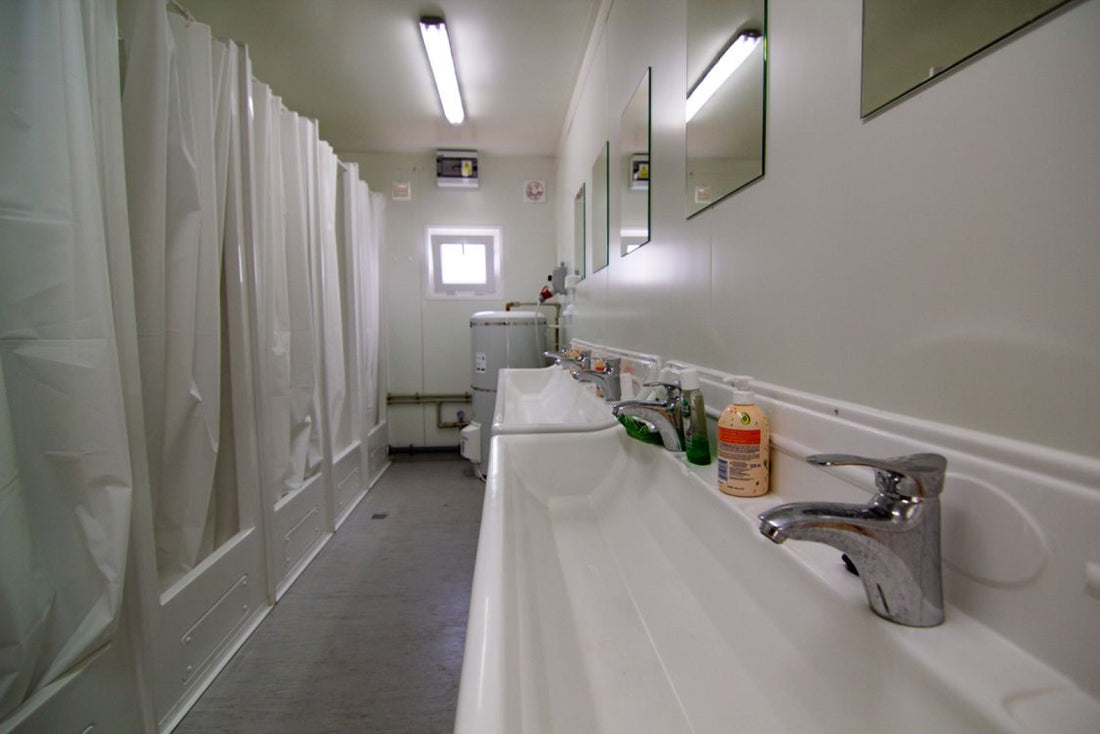 Row of shared public shower stalls with wet tiled floors in a locker-room setting