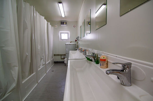 Row of shared public shower stalls with wet tiled floors in a locker-room setting