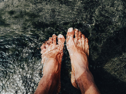 Bare feet with unpainted toenails standing in clear shallow water over dark stone