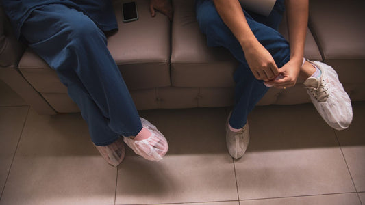 Two healthcare workers in scrubs and protective shoe covers
