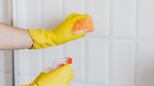 Gloved hands cleaning white bathroom tiles with spray