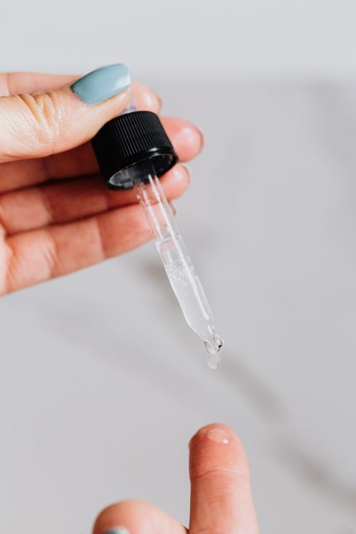 Clear liquid dripping from a glass dropper onto a fingertip