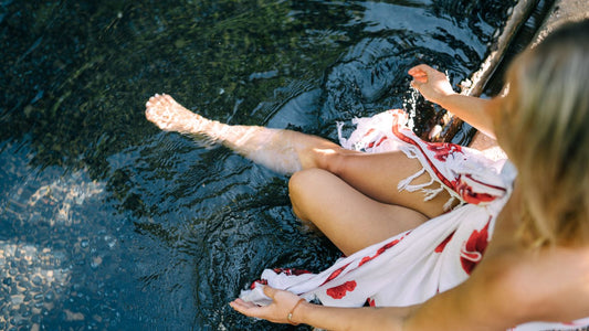 Person sitting by water dipping their feet in