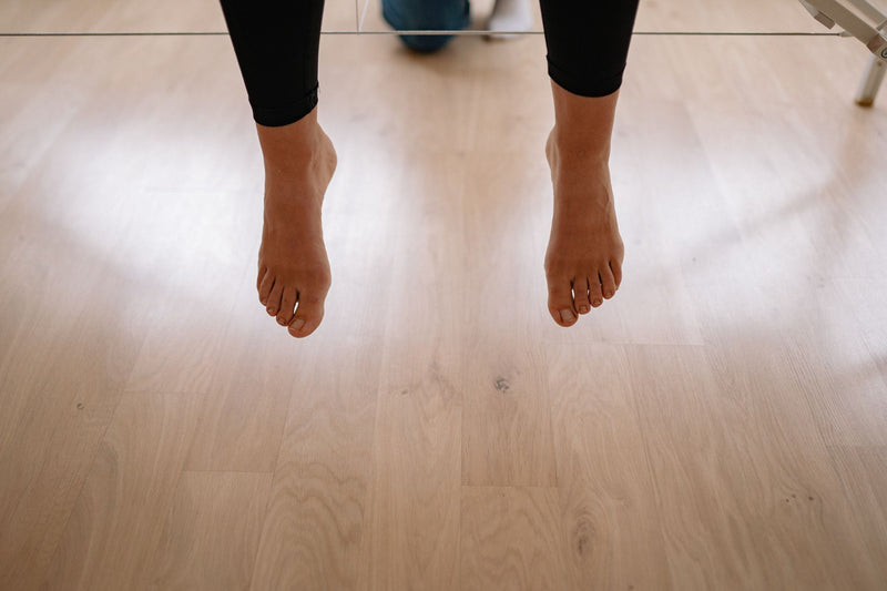 Bare feet above a wooden floor with toenails in view, the angle for spotting a nail lifting from its bed
