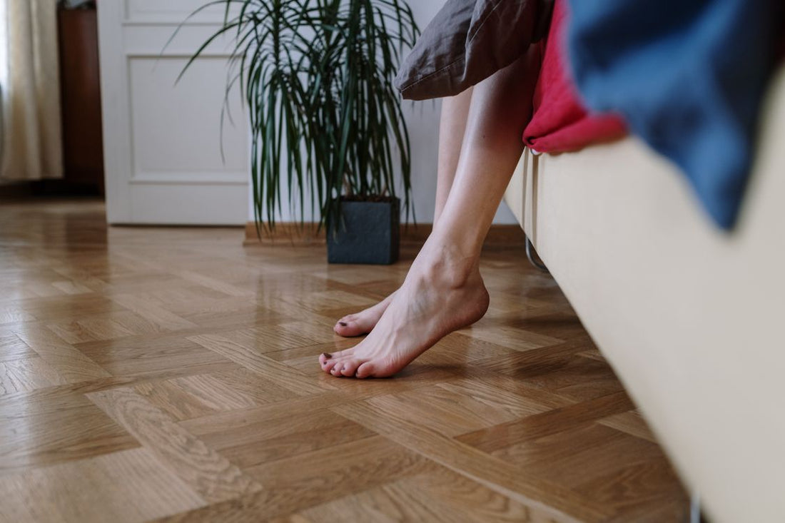 A person's bare feet resting on a wooden floor in a calm indoor setting