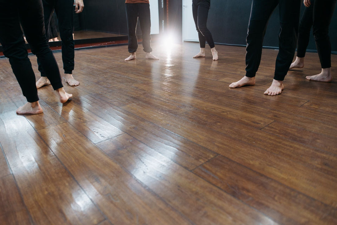 Bare feet on a polished wooden studio floor, where repeated impact can bruise or darken a toenail