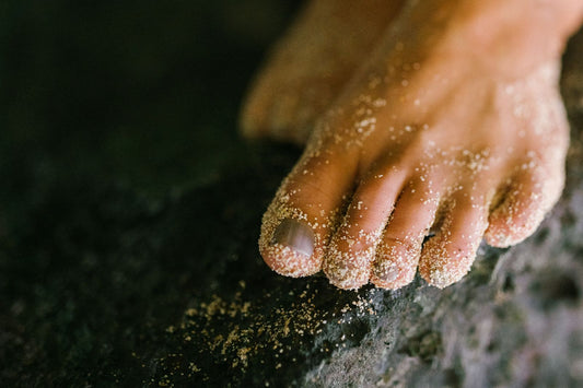 Close-up of bare toes and unpainted toenails dusted with sand, resting on a dark rock
