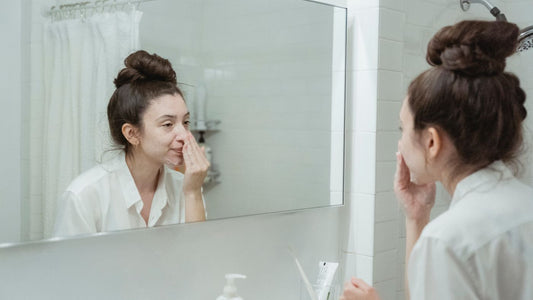 Woman applying skincare in a bathroom mirror, illustrating a routine change that can trigger purging