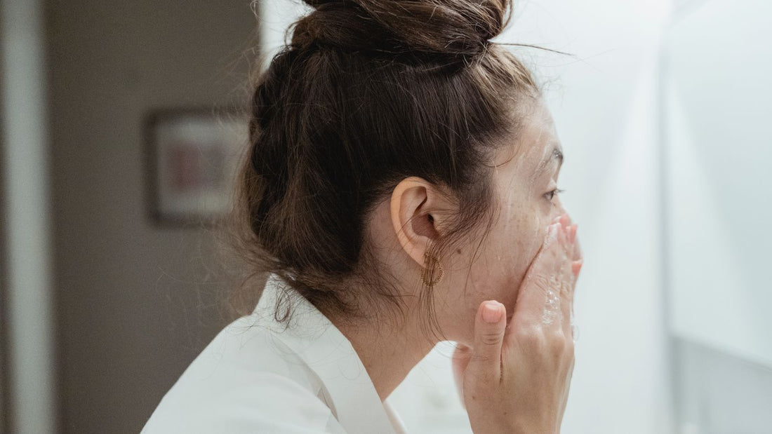 Person in a bathrobe washing their face at a bathroom sink