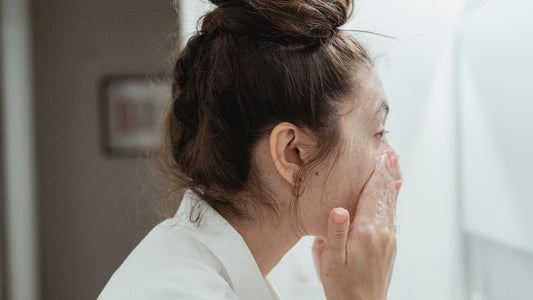 Person in a bathrobe washing their face at a bathroom sink
