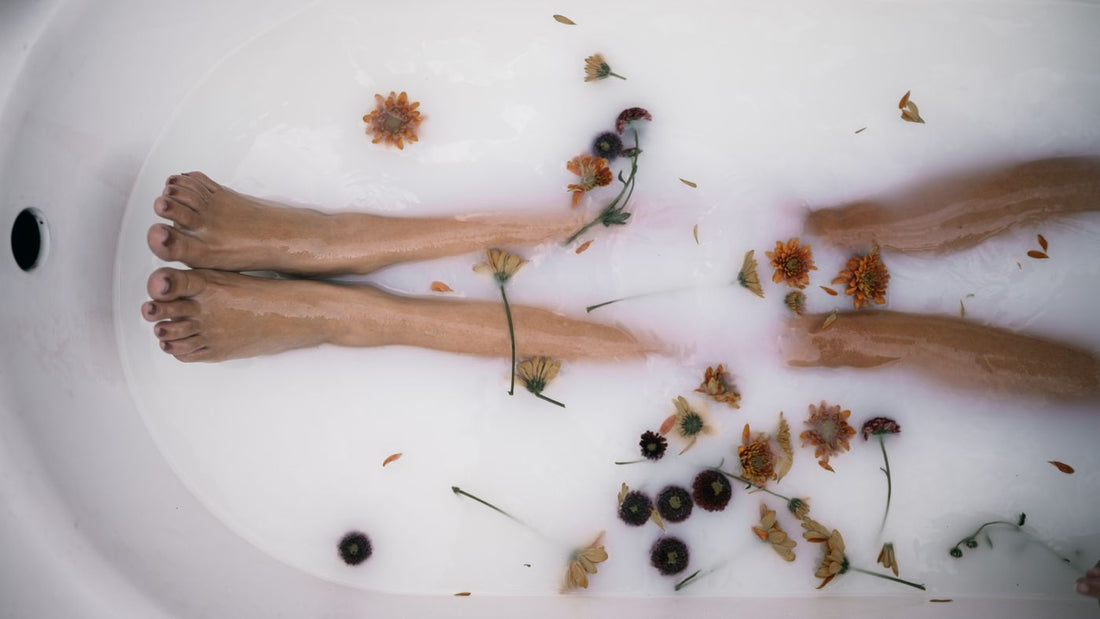 Legs resting in a warm foot bath with floating petals