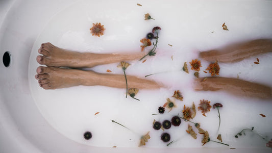 Legs resting in a warm foot bath with floating petals