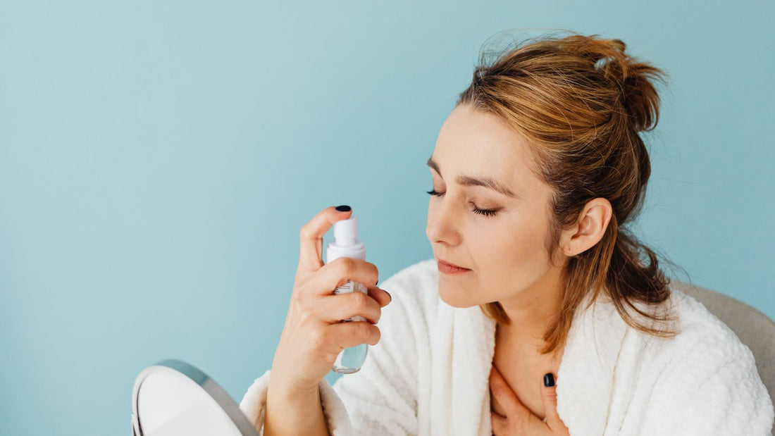 Woman in a white robe spraying a facial mist onto her face, illustrating a comparison of hypochlorous acid sprays and an iodine mist